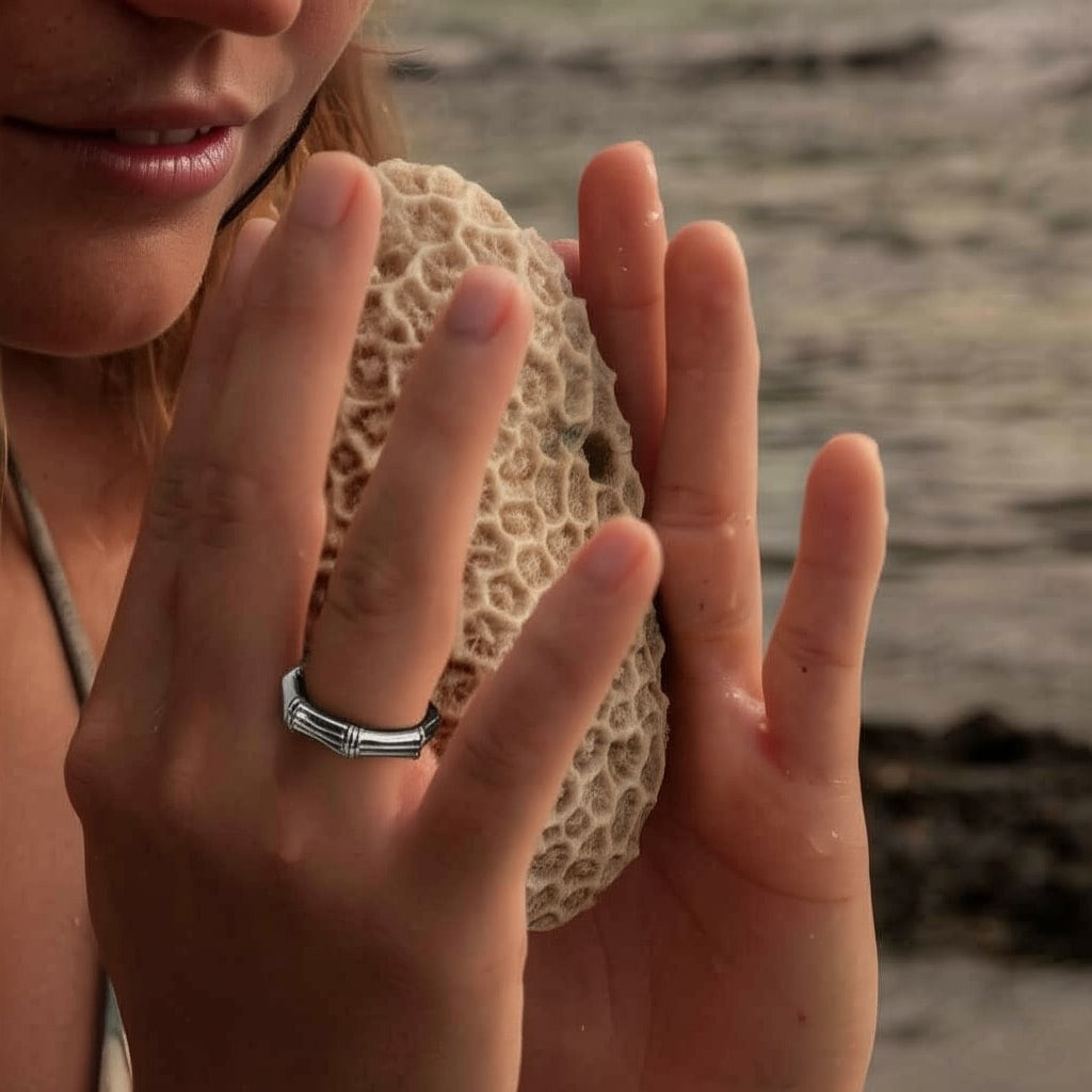 Close-up of a woman's hands holding natural coral by the sea, wearing a bold silver ring – capturing EQUØRA’s harmony of strength, texture, and organic beauty.
