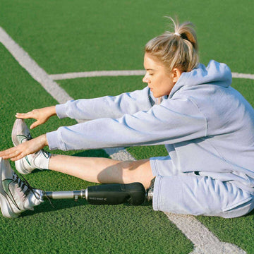 Focused woman with prosthetic leg stretching on a sports field – expressing determination, grace, and empowered movement.