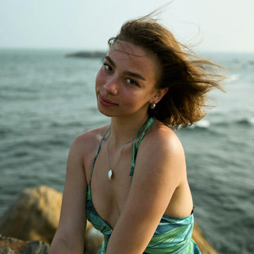 Woman wearing shell jewellery and a green halter dress by the sea – reflecting calm confidence, nature-led femininity, and inner clarity.
