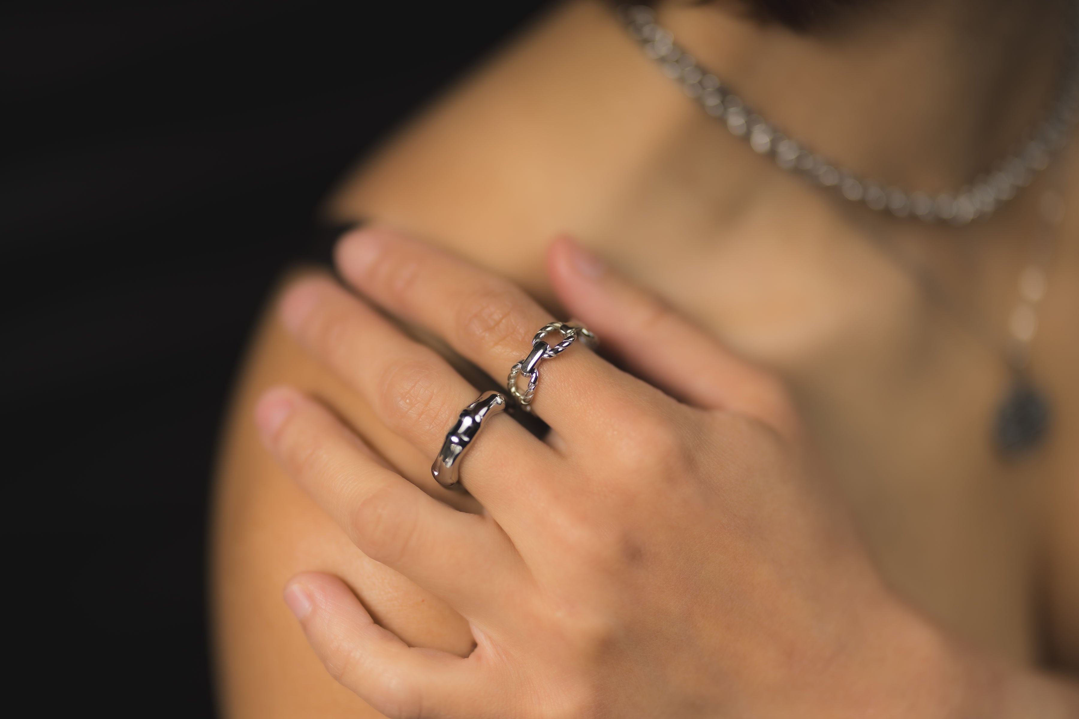Model wearing EQUØRA silver rings, hoop earrings, and layered chain necklaces, posing with hand on head against a dark, modern background for a sleek and minimal look.