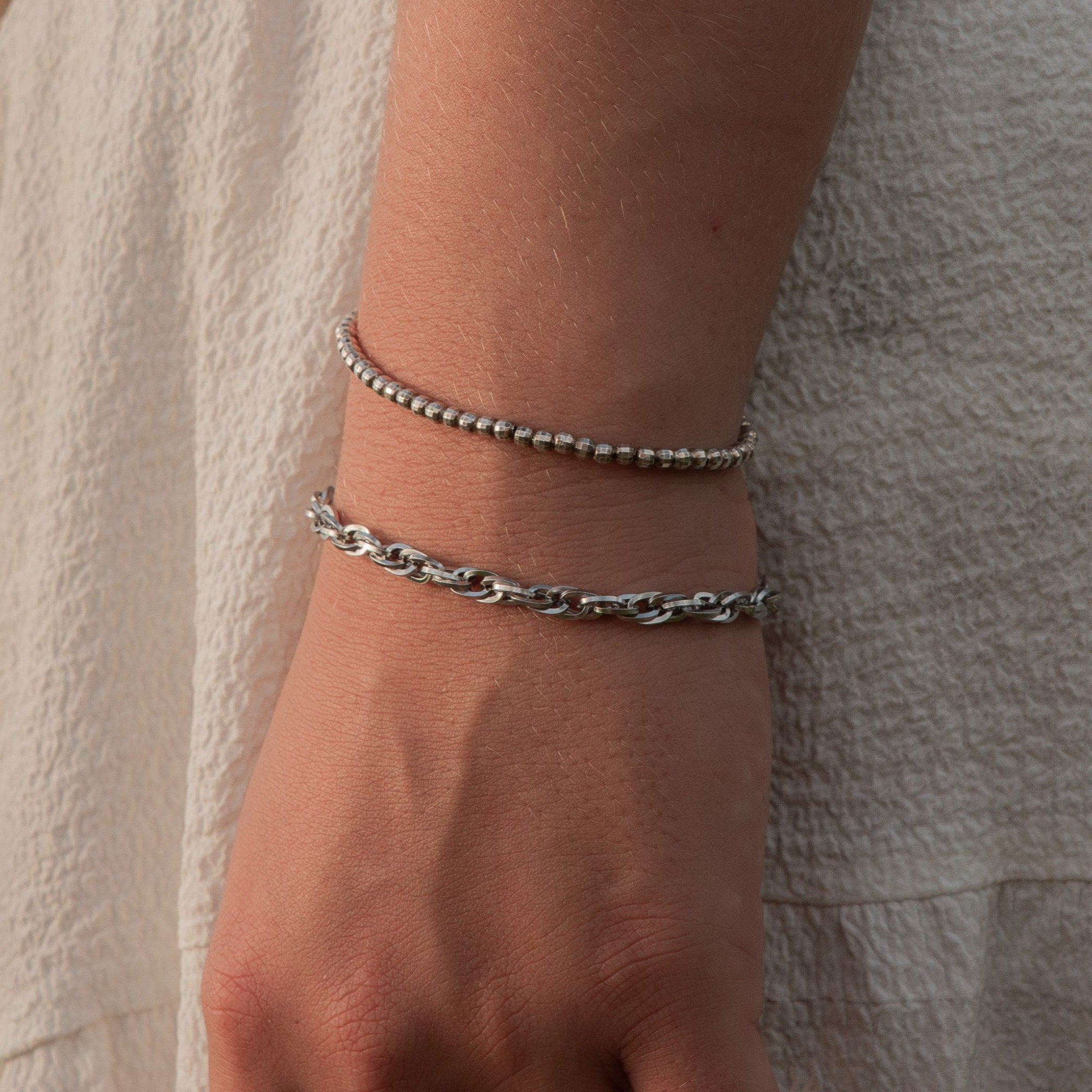 Close-up of a woman’s wrist wearing layered silver chain and beaded bracelets – showcasing EQUØRA’s signature blend of strength, simplicity, and everyday elegance.