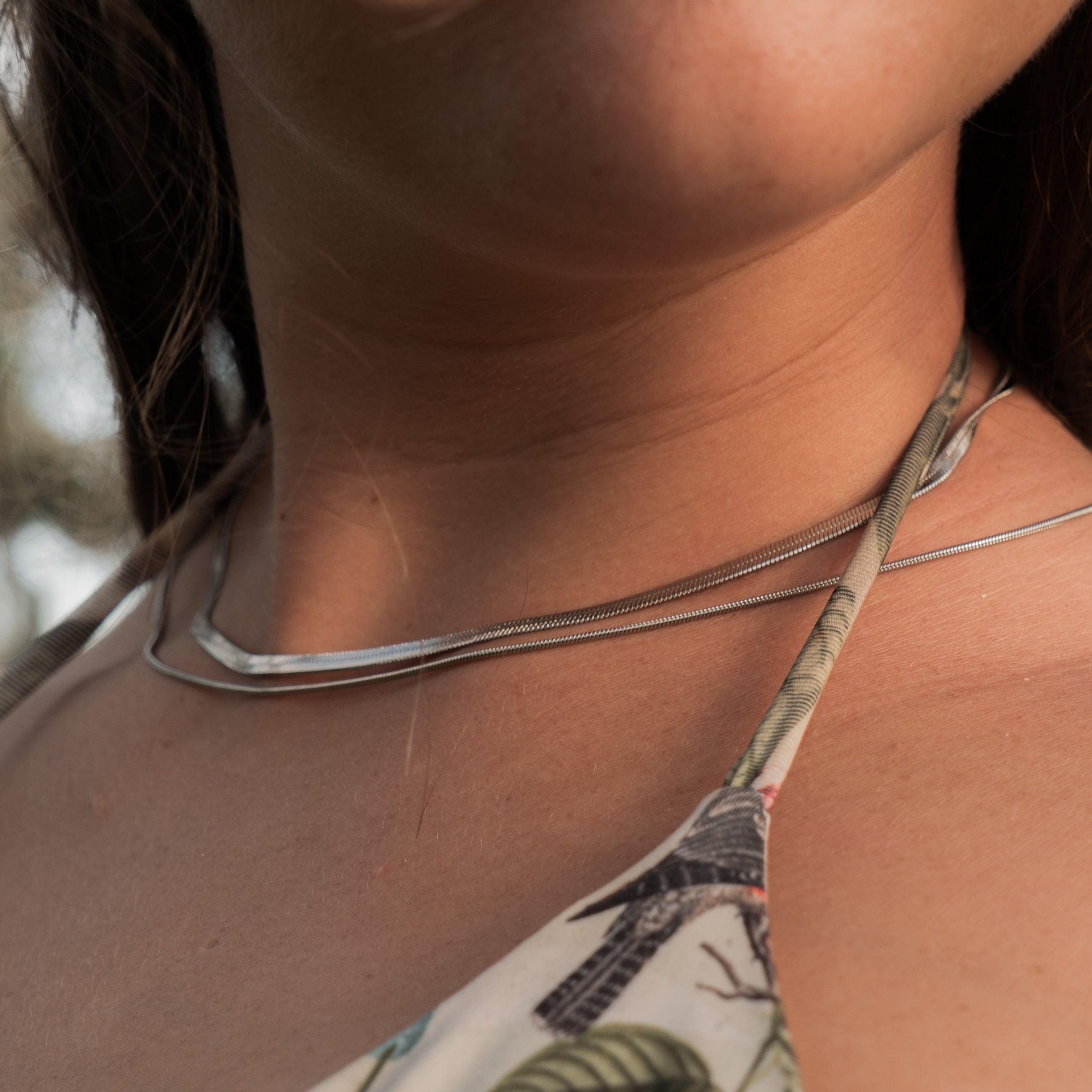 Close-up of layered silver necklaces resting on a woman's collarbone, styled with a tropical halter top – expressing EQUØRA’s signature of subtle strength and fluid femininity.
