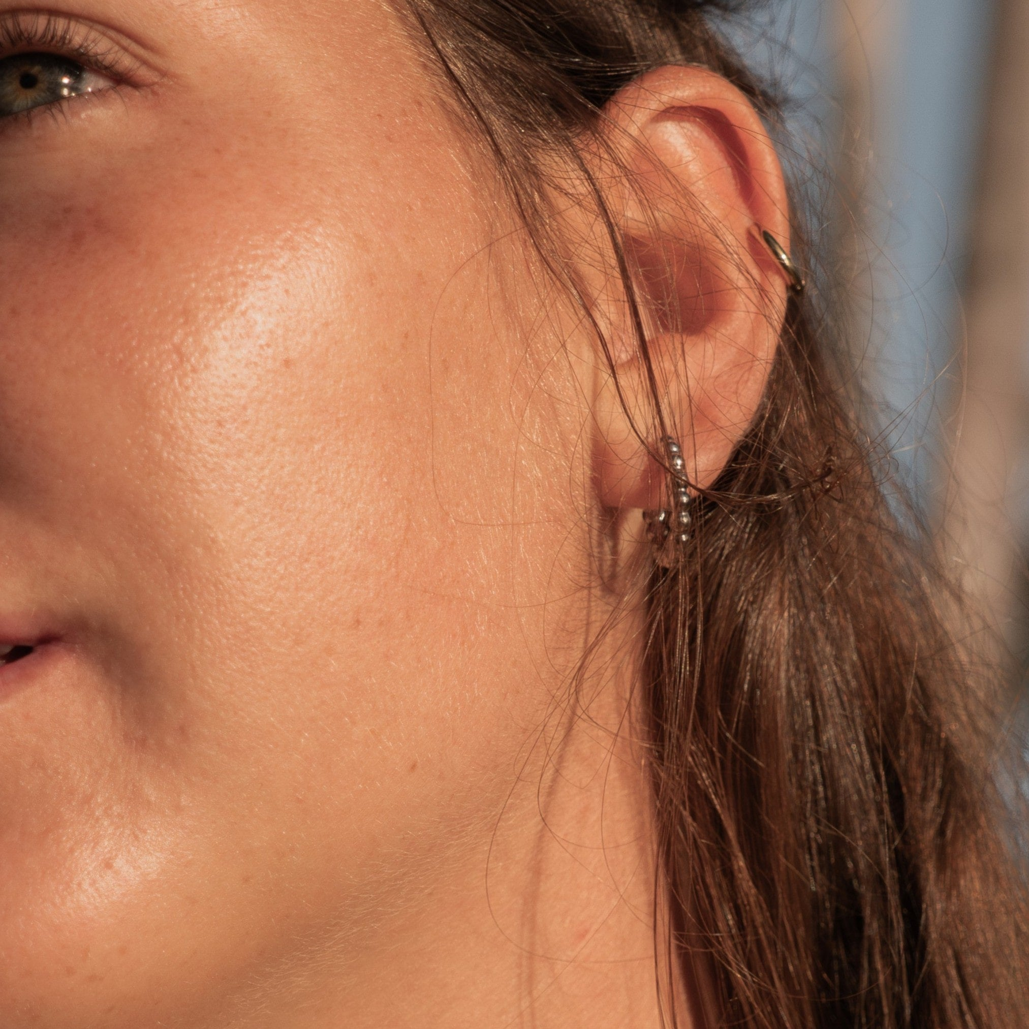 Close-up of a woman's ear wearing layered silver earrings and a gold cuff – highlighting EQUØRA’s refined contrasts and movement-ready minimalism.