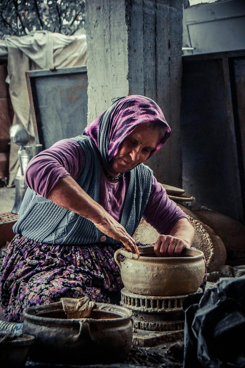 Elderly woman shaping clay by hand in a rustic workshop, dressed in traditional clothing – honouring generational craftsmanship, quiet skill, and enduring strength.