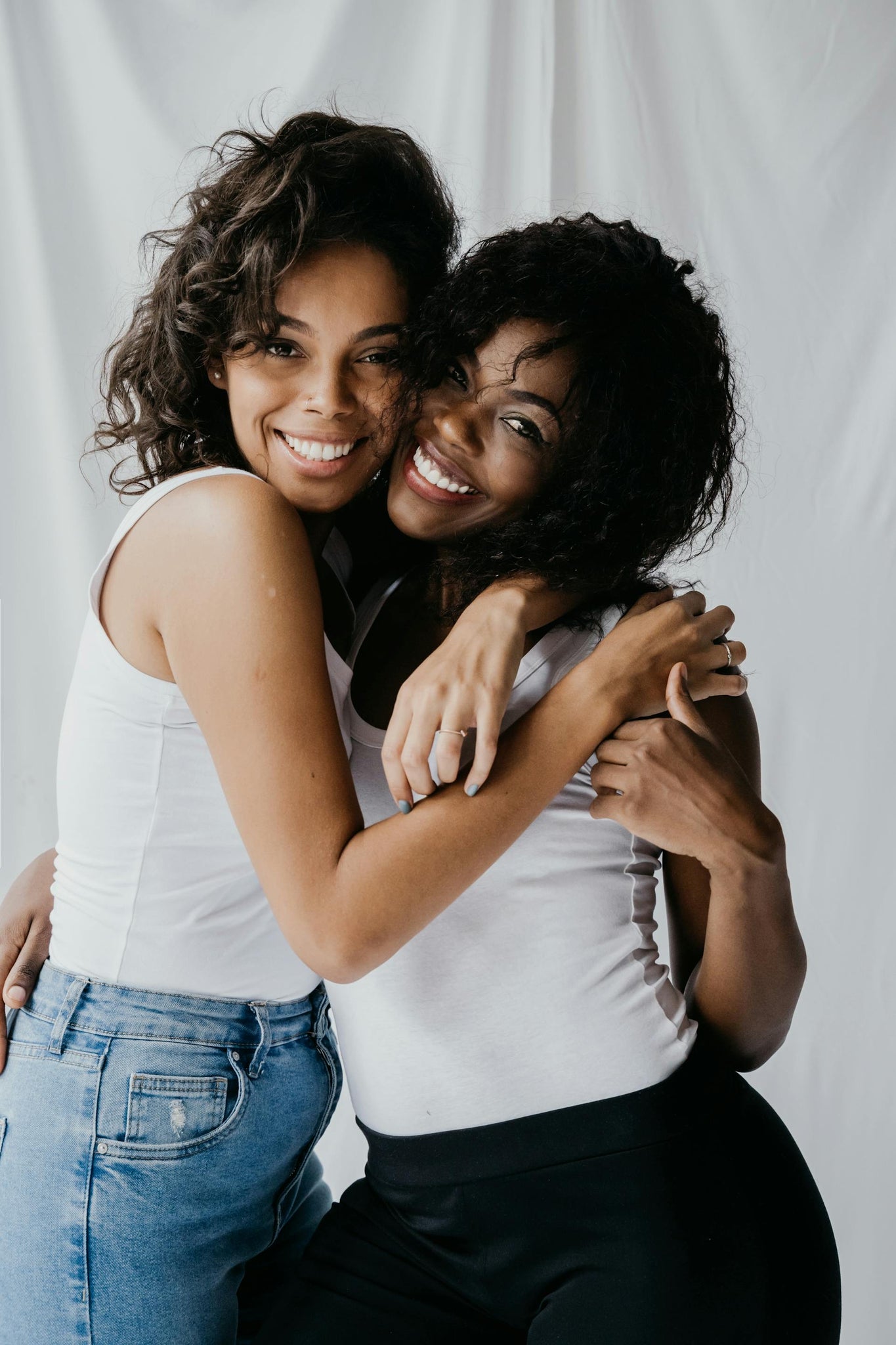 Two women embracing and smiling in casual wear against a white backdrop – representing EQUØRA’s affiliate community built on connection, authenticity, and shared purpose.