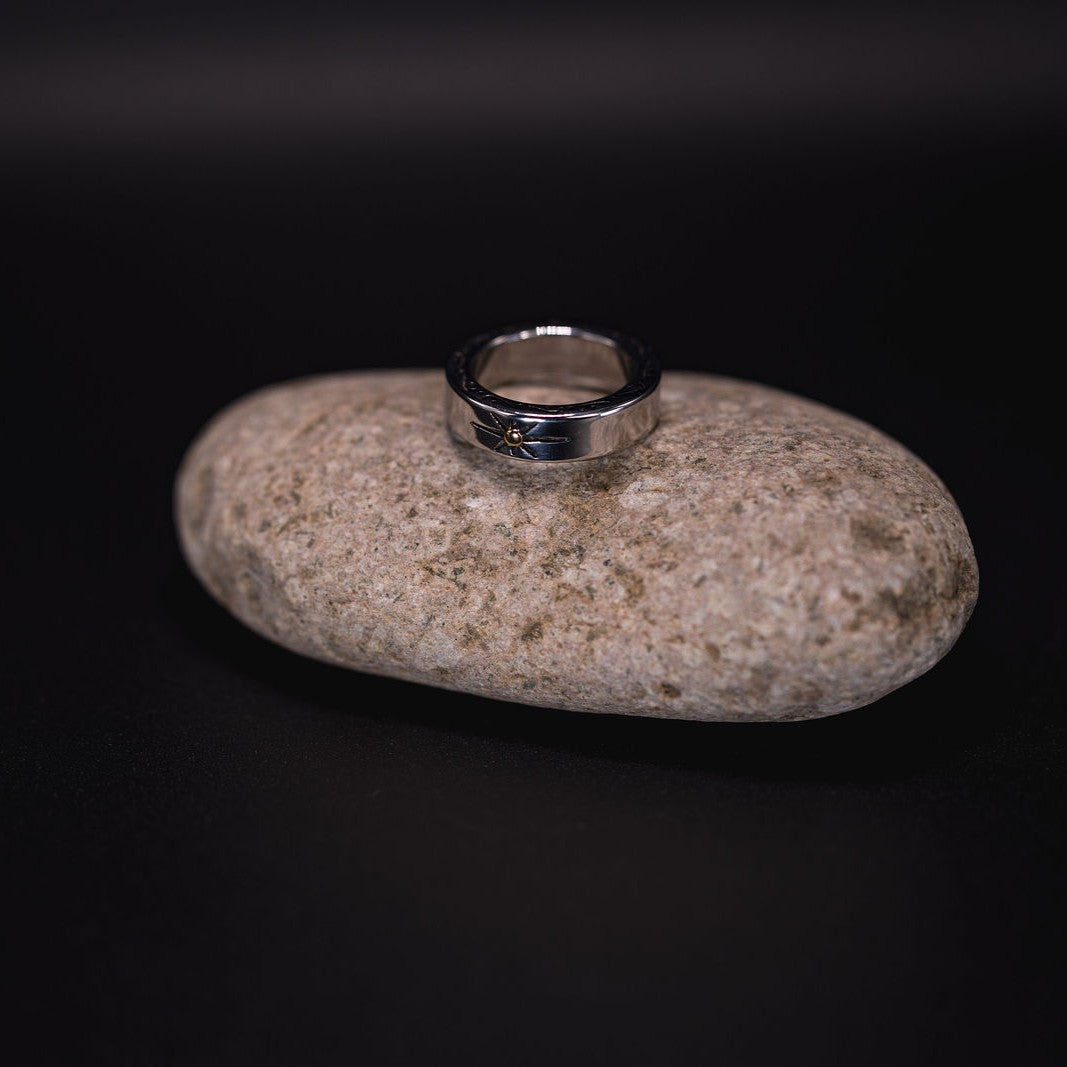 EQUØRA Auryn Totem Ring — bold silver-tone band with intricate engraved detailing, resting on a smooth stone backdrop. A unisex statement piece inspired by ancient symbolism and coastal design.
