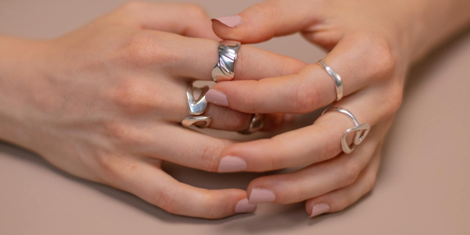 Close-up of hands wearing multiple silver rings on nude pink nails – illustrating EQUØRA’s daily-wear jewellery and care essentials for long-lasting shine and strength.