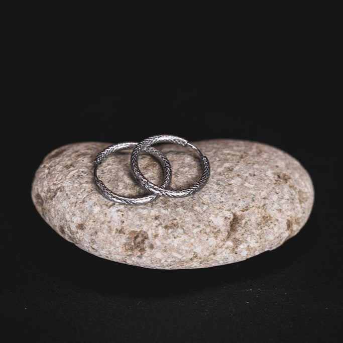 EQUØRA Coil Earrings in textured stainless steel, bold twisted hoop design laid on a natural stone — hypoallergenic, tarnish-resistant statement jewellery for everyday wear.