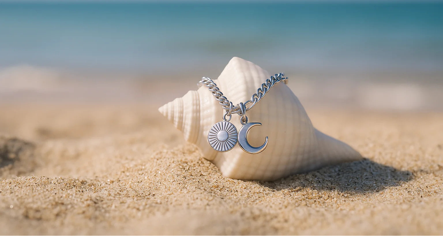 Silver sun and moon charm bracelet draped over a seashell on the sand – symbolising connection, calm, and EQUØRA’s invitation to reach out with intention.