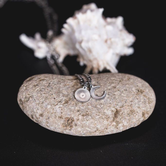 EQUØRA Dreamer Necklace featuring sun and moon pendants, styled on a natural stone with a seashell backdrop — celestial-themed stainless steel jewellery inspired by coastal serenity.