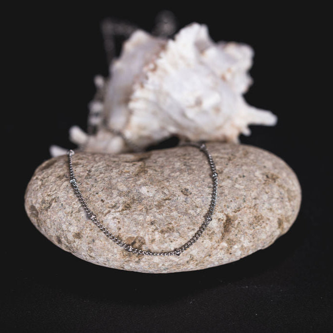 EQUØRA Dune Necklace with textured silver bead detail, styled over a natural stone and seashell backdrop — understated coastal-inspired jewellery for daily wear.