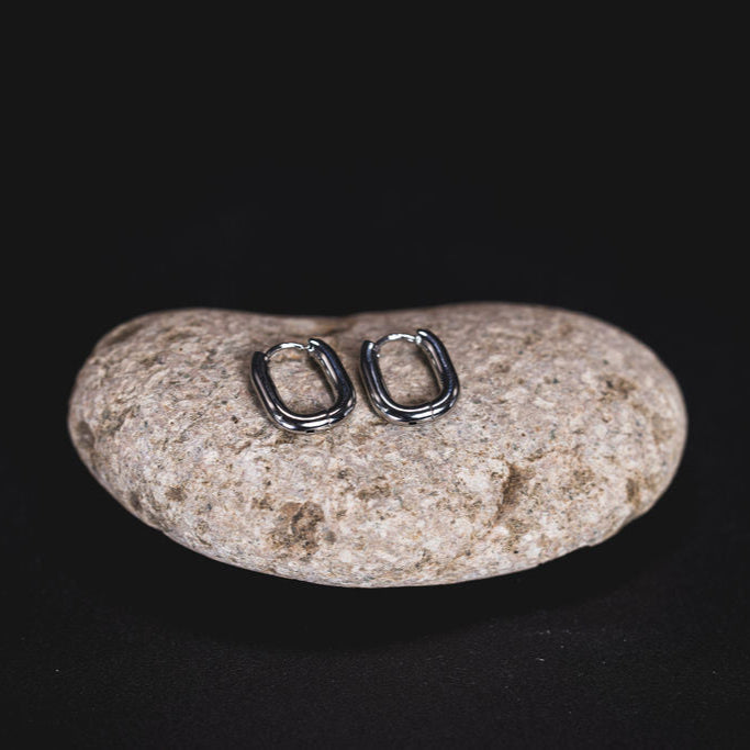 EQUØRA Ellix Earrings — chunky oval silver hoops with a polished finish, handcrafted in stainless steel and displayed on a natural stone. Bold, durable, and water-friendly design.