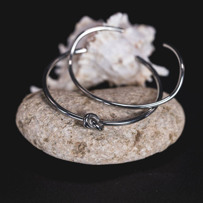 EQUØRA Knotion and Möbius Bracelet — sleek silver cuff bracelet with a central knot detail, displayed on a natural stone. A symbolic piece representing unity and fluid design, ideal for everyday minimal style.