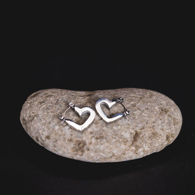 EQUØRA Luma Earrings — heart-shaped silver hoops with organic curves, crafted in stainless steel and styled on a smooth beach stone. Lightweight, romantic, and water-resistant.