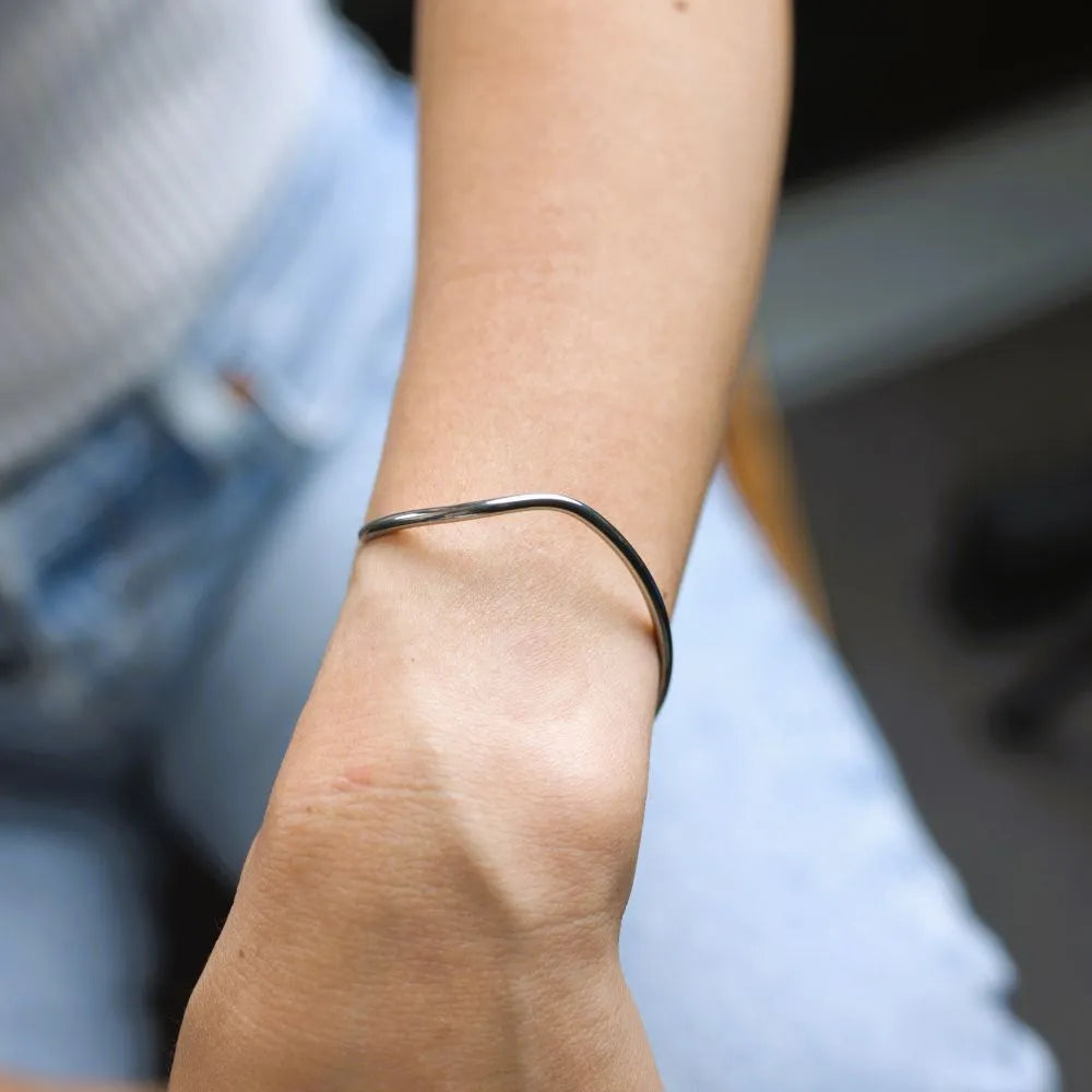 Curved silver Möbius bracelet laid flat – showcasing sculptural elegance inspired by infinite loops and inner balance.
