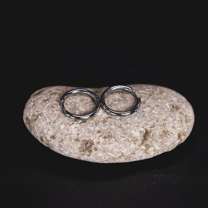EQUØRA Orbit Earrings — polished stainless steel minimalist hoop earrings resting on a natural stone. Timeless circular design for everyday wear.