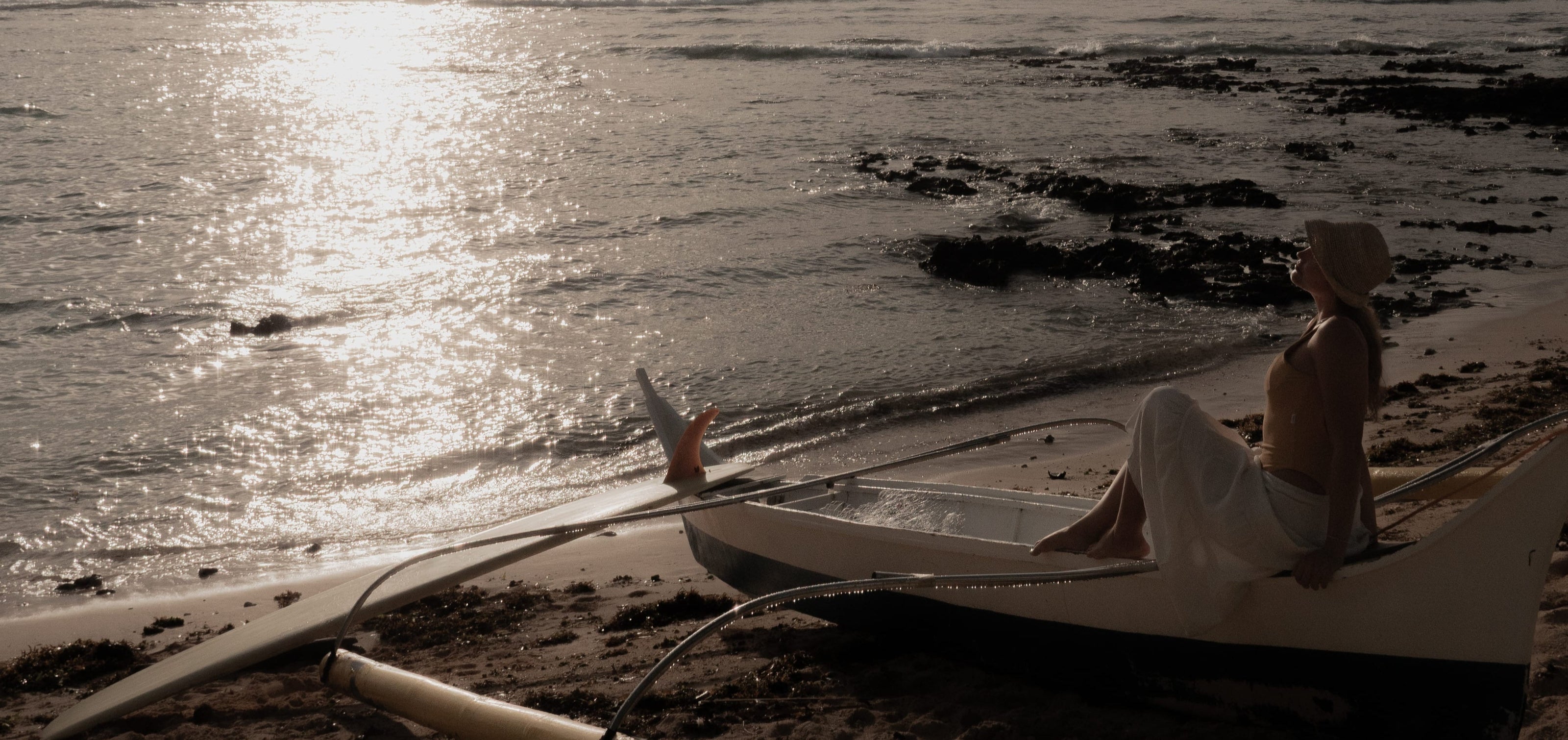 Woman sitting on a traditional boat at sunset, gazing over the ocean – reflecting EQUØRA’s journey of intention, quiet strength, and timeless movement.
