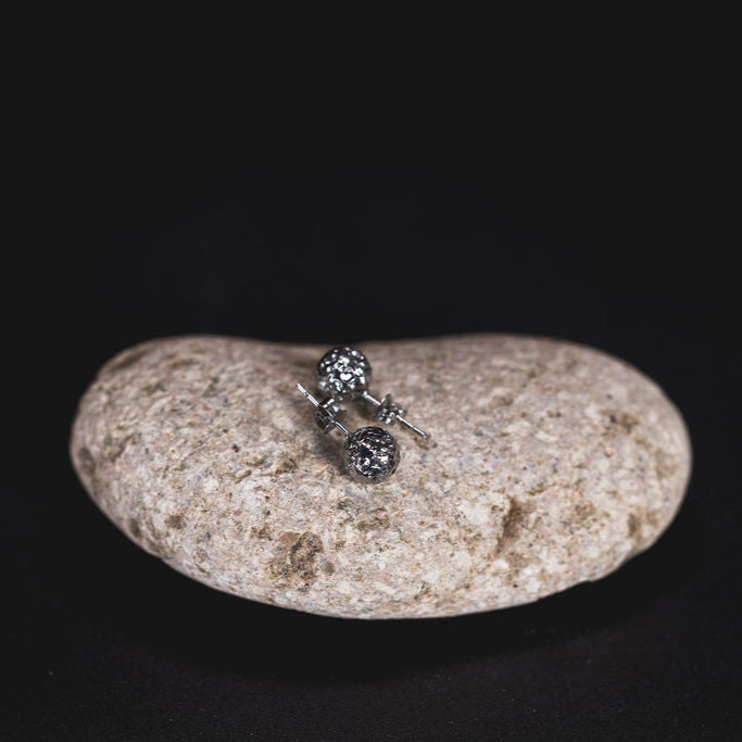 EQUØRA Sol Earrings — stainless steel stud earrings with textured sun-inspired spherical design, displayed on a natural stone. Hypoallergenic and nickel-free minimalist jewellery.