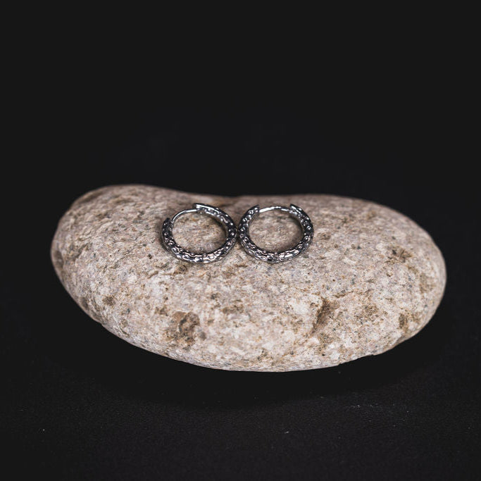 EQUØRA Terra Earrings — full textured hoop earrings in stainless steel with a hammered organic surface, resting on a smooth stone. Water-safe and tarnish-resistant everyday jewellery.