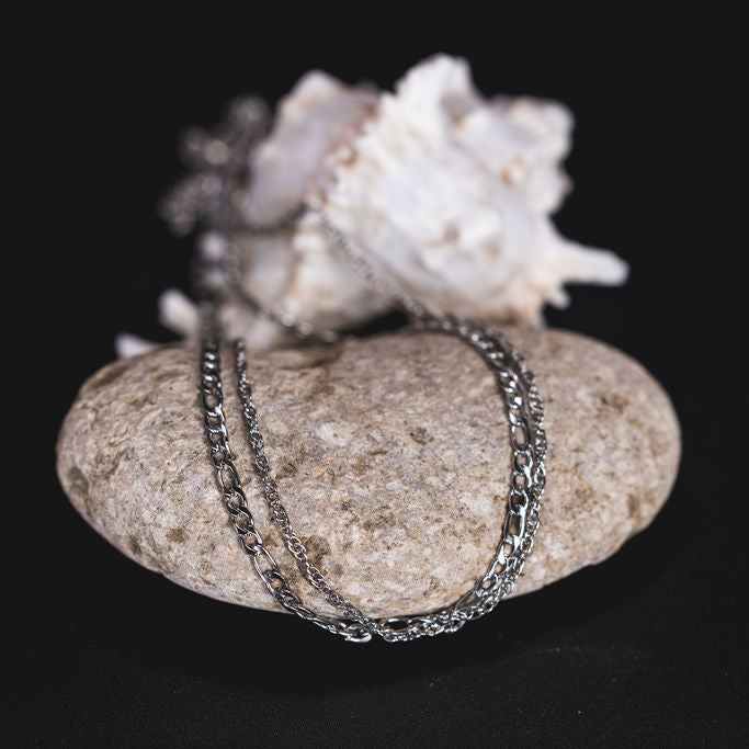 EQUØRA Tide Necklace featuring layered stainless steel chains, displayed on a smooth stone with a natural seashell — modern ocean-inspired jewellery design for everyday wear.