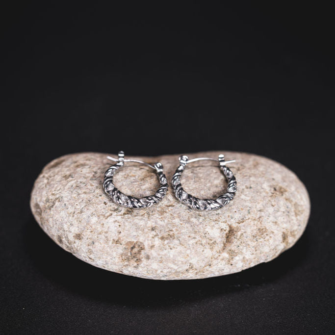 EQUØRA Twine Earrings featuring intricately braided stainless steel hoops, displayed on a natural stone — lightweight, water-safe, and hypoallergenic for modern everyday wear.