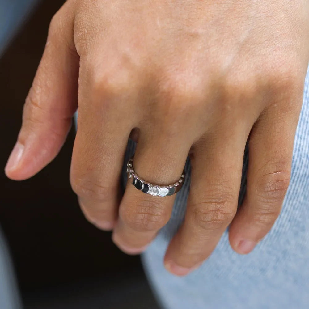Close-up of a hand wearing a waveform ring with a blurred outdoor background – a soft yet strong statement of continuous flow.